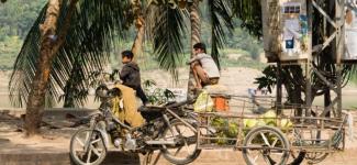 Laos image of motorcycle, cart and people on the street surrounded by palm trees