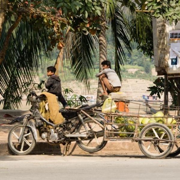 Laos image of motorcycle, cart and people on the street surrounded by palm trees